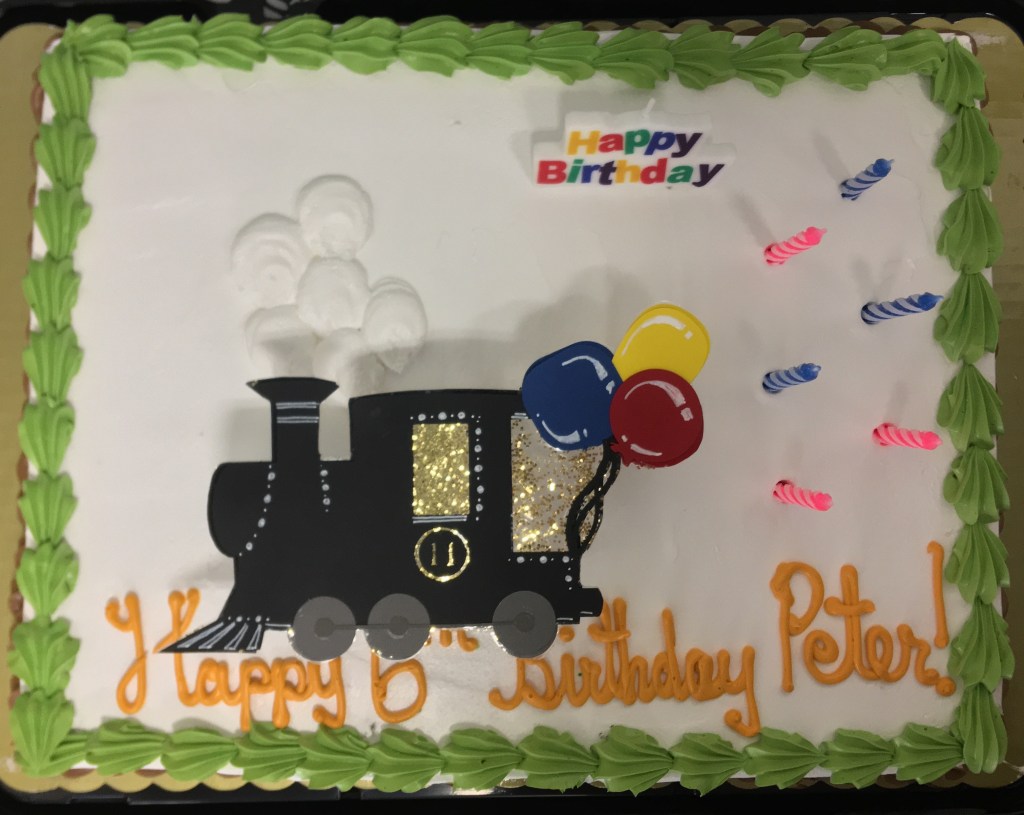 The Cardstock Train sits ontop of the cake with a cluster of white balloons behind the smoke stack.